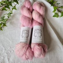 Load image into Gallery viewer, Two pink skeins of yarn with labels on a white fabric background with greenery.
