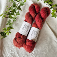 Load image into Gallery viewer, Three skeins of red yarn with labels on a textured white surface with green leaves.